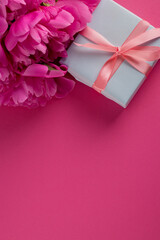 Bouquet of Pink Peonies near a blue gift box tied by a gentle silk bow on a magenta color background with empty space for text. Good for Womens day, Mothers day festive banner background.