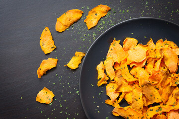 Healthy sweet potato chips on dark wood background