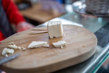 Kostka białego sera na tacy. Biały ser na drewnianej tacy. A cube of white cheese on a tray. White cheese on a wooden tray.