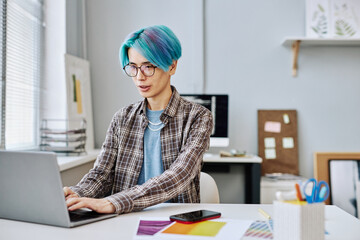 Portrait of creative young man with blue hair using laptop in office, copy space
