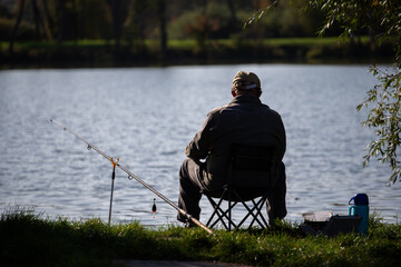Wędkarz siedzący na brzegu. Wędkarz czekający na rybę. Angler sitting on the shore. Angler waiting for a fish. - obrazy, fototapety, plakaty