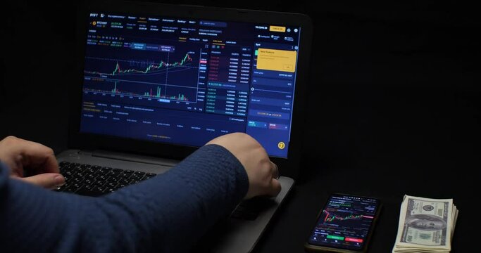 Nervously twisting bitcoin in his hand, a man bets on a stock of cryptocurrencies on a laptop. Rise and fall chart of cryptocurrency on laptop screen. The concept of buying cryptocurrency.