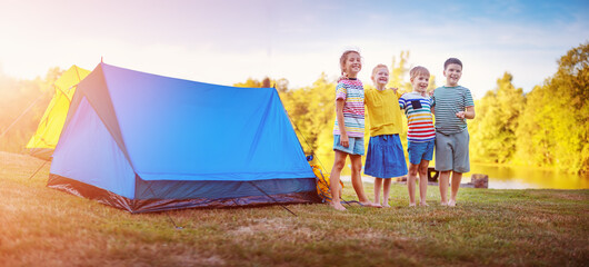 Group of four children standing near colourful tents in nature.
