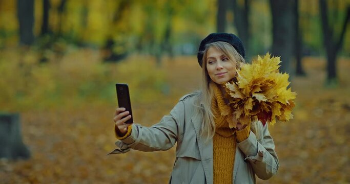 woman taking selfie by smartphone in beautiful autumn park, posing with leaves bunch, 4K, Prores