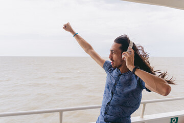 Young latin man with long hair wearing headphones while shouting with clenched fist towards the Rio de la Plata.