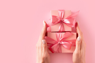 Womans hands holding wrappes gift box with ribbon on pink background