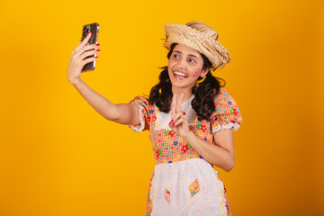 Beautiful brazilian woman, with festa junina clothes, taking self portrait with smartphone.