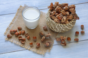 Nut milks. Glass of dairy-free alternative milk,  hazelnuts in small basket on rustic table
