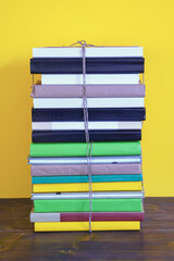 Stacks of different books tied with rope on rustic table. Yellow background, copy space
