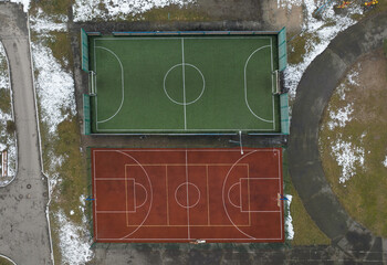 Obraz premium A football field and a tennis court in winter, shot vertically by a drone. There is snow on the sides of the field