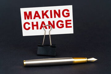 On the black surface is a pen, an office paper clip with a business card on which is written - MAKING CHANGE