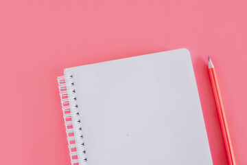 Notebook with a blank page and a pencil on pink background.