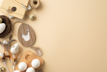 Vintage Easter concept. Top view photo of rustic decor easter eggs in wooden holder nest ceramic bunny drawing block paintbrushes twine and quail feathers on isolated beige background with empty space