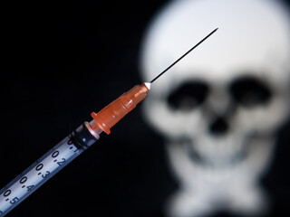 A vaccine syringe with needle in front of black background with abstract skulls