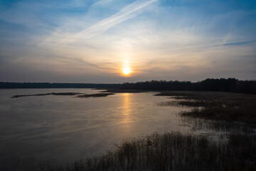 Fototapeta na wymiar Sunset reflection in frozen lake. Brirds flying over sunset reflection sky. Cloudy sunset sky reflection