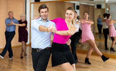 Fototapeta na wymiar Dynamic middle-aged pair engaging in Latino dance in dance studio. Pairs training ballroom dance in hall