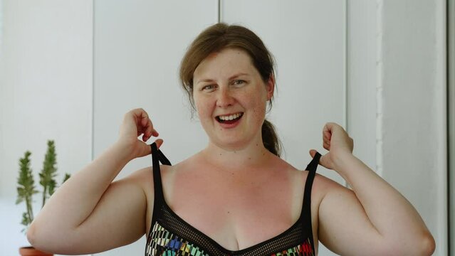 Portrait of pale-skinned woman with freckles on face taking off bra straps with burnt skin. Woman in severe pain looks at camera. Red sunburns on delicate skin of decollete, pale spots from swimsuit.