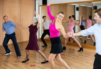 Dynamic middle-aged pair engaging in ballroom dance in dance studio. Pairs training ballroom dance in hall