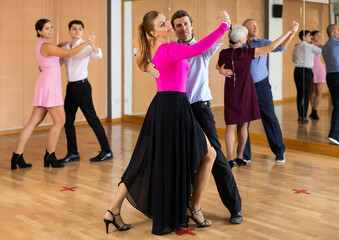 Fototapeta na wymiar Active middle-aged pair practicing ballroom dance in training hall during dancing-classes. Pairs training ballroom dance