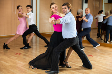 Positive adult couple enjoying slow foxtrot in dance studio. Amateur social dancing concept..