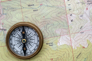 Topographical map showing contour lines with classic compass laid on top, flat lay