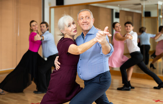 Active elderly pair practicing ballroom dance in training hall during dancing-classes. Pairs training ballroom dance