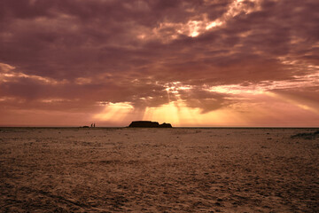 backlit couple running at sunset on the beach with pink clouds in the sky and an island in the background