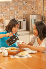 Asian young lady serving coffee on breakfast to her sister at the kitchen.