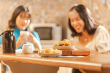 Cheese breads on the table with girls having breakfast behind. (Pao de queijo)