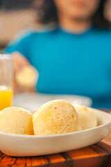 Cheese breads on the table with a girl having breakfast behind. (Pao de queijo)
