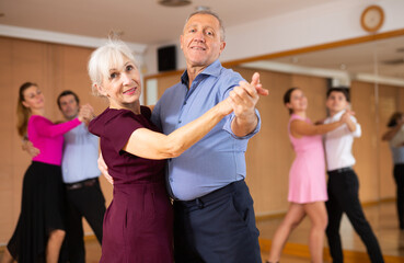 Cheerful elderly couple practicing ballroom dances in ballroom