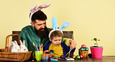 Father and son painting Easter eggs. Cute little child boy wearing bunny ears on Easter day. Happy Easter family painting eggs for holidays. Father and little child boy preparing for Easter holiday.