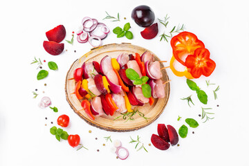 Raw chicken leg meat skewers with vegetables,plums,peppers,onions, on a white background.Uncooked mixed meat skewer with peppers.Skewers with pieces of raw meat, red, yellow and green pepper.Top view.