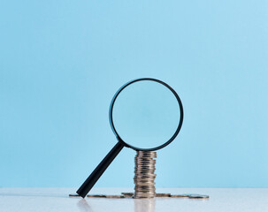 A stack of metal coins and a plastic magnifier on a blue background. The concept of increasing...