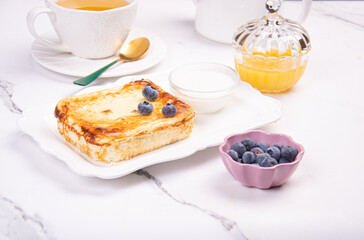 Cottage cheese casserole with blueberries and honey on a white table. Breakfast.