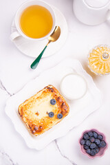 Cottage cheese casserole with blueberries and honey on a white table. Breakfast.