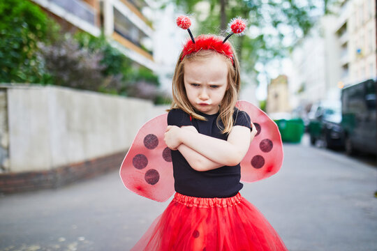 Moody preschooler girl in ladybug costume on a street