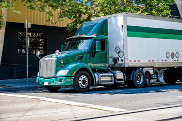 Dark green day cab big rig semi truck with roof spoiler make delivery of the cargo stocked in dry...