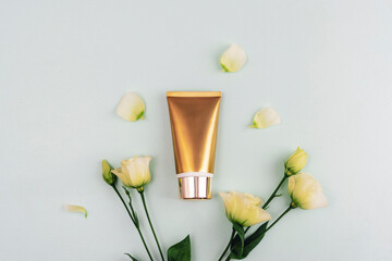 Golden cream tube and white eustoma flowers on light blue background. Top view, flat lay, mockup