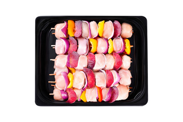 Skewers with pieces of raw meat, red, yellow and green pepper.Raw chicken skewers of fillet with vegetables, plums, peppers, onions, in a tray on a white background. Close-up.Top view.