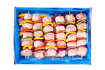 RSkewers with pieces of raw meat, red, yellow and green pepper.aw chicken skewers with vegetables, peppers,plums,onions, in a cardboard box on a white background. Close-up.Top view.