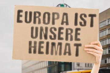 The phrase " Europe is our home " is on a banner in men's hands with blurred background. Tolerance. Acceptance. Democracy. Peace.  Change. Voice. Power. Social. Political. Movement. Citizen. Awareness