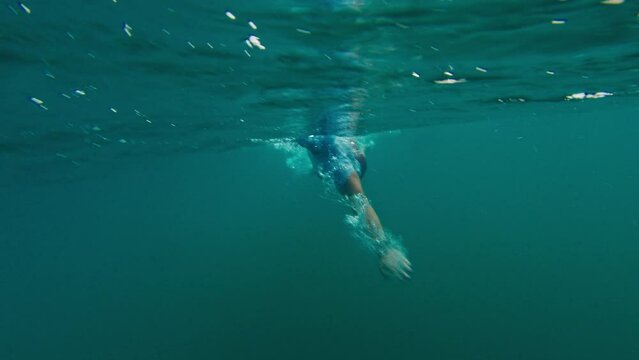 Man swims in the open sea. Underwater of the swimmer strokes in the ocean