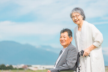 公園で車椅子に乗って散歩する高齢者夫婦（シニア・男女）
