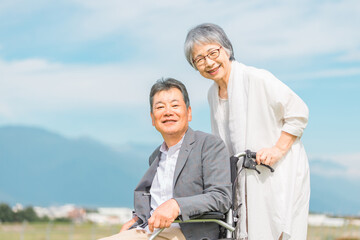 公園で車椅子に乗って散歩する高齢者夫婦（シニア・男女）
