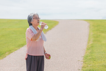 公園で水を飲みながら深呼吸する高齢者女性
