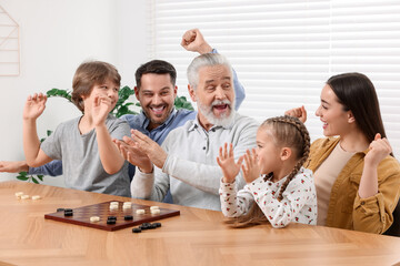 Emotional family playing checkers at wooden table in room
