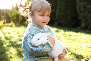Cute little girl with adorable rabbit outdoors on sunny day