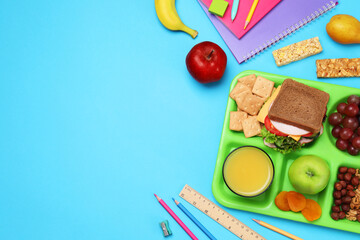 Flat lay composition with tray, tasty food and school stationery on light blue background. Space...