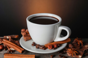Cup of delicious hot chocolate, spices and coffee beans on wooden table